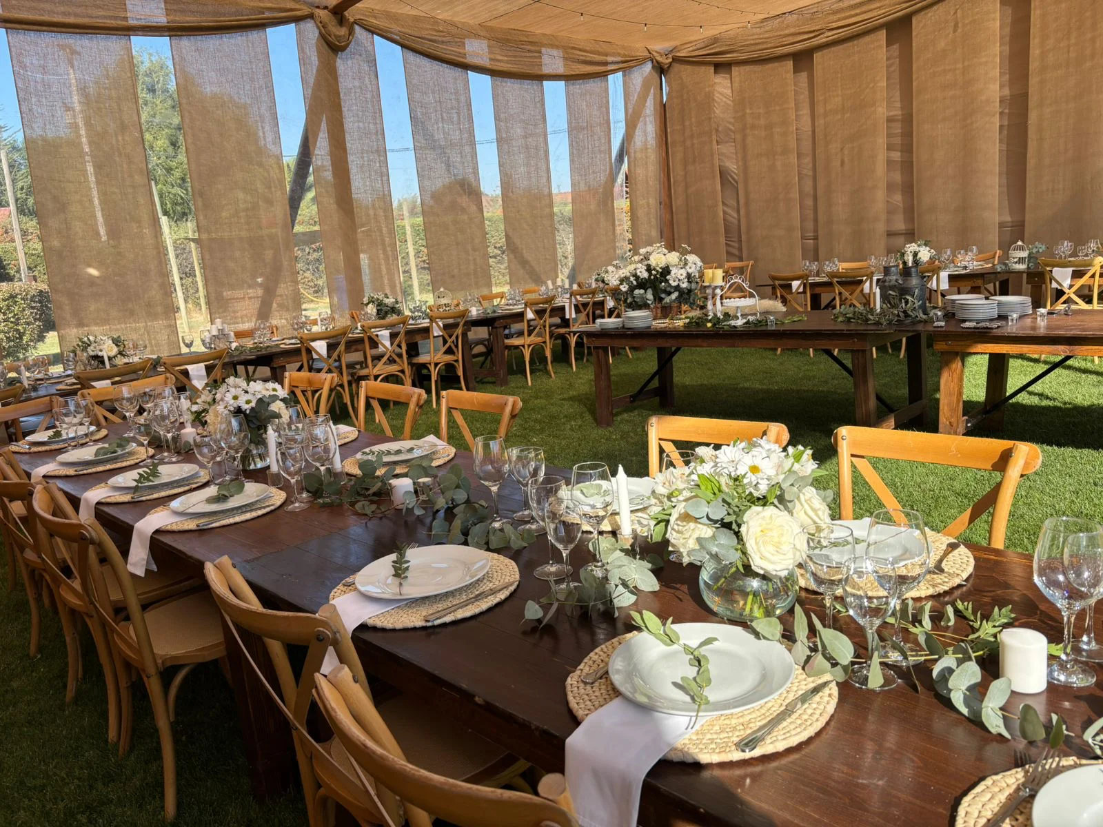 Mesas largas decoradas con eucalipto y rosas blancas bajo una carpa rústica para un banquete de matrimonio en Santiago