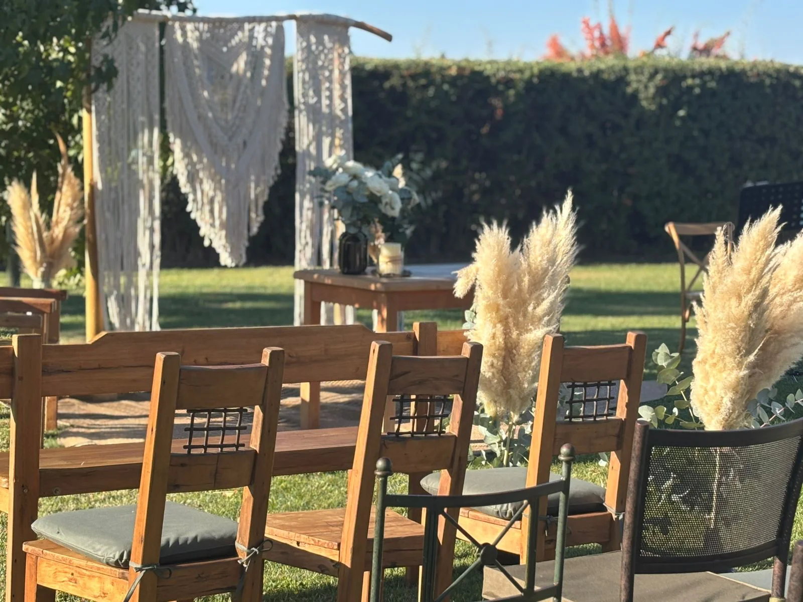 Ceremonia al aire libre con sillas de madera, telón de macramé y pampas grass en un evento decorado por Matías al Fuego