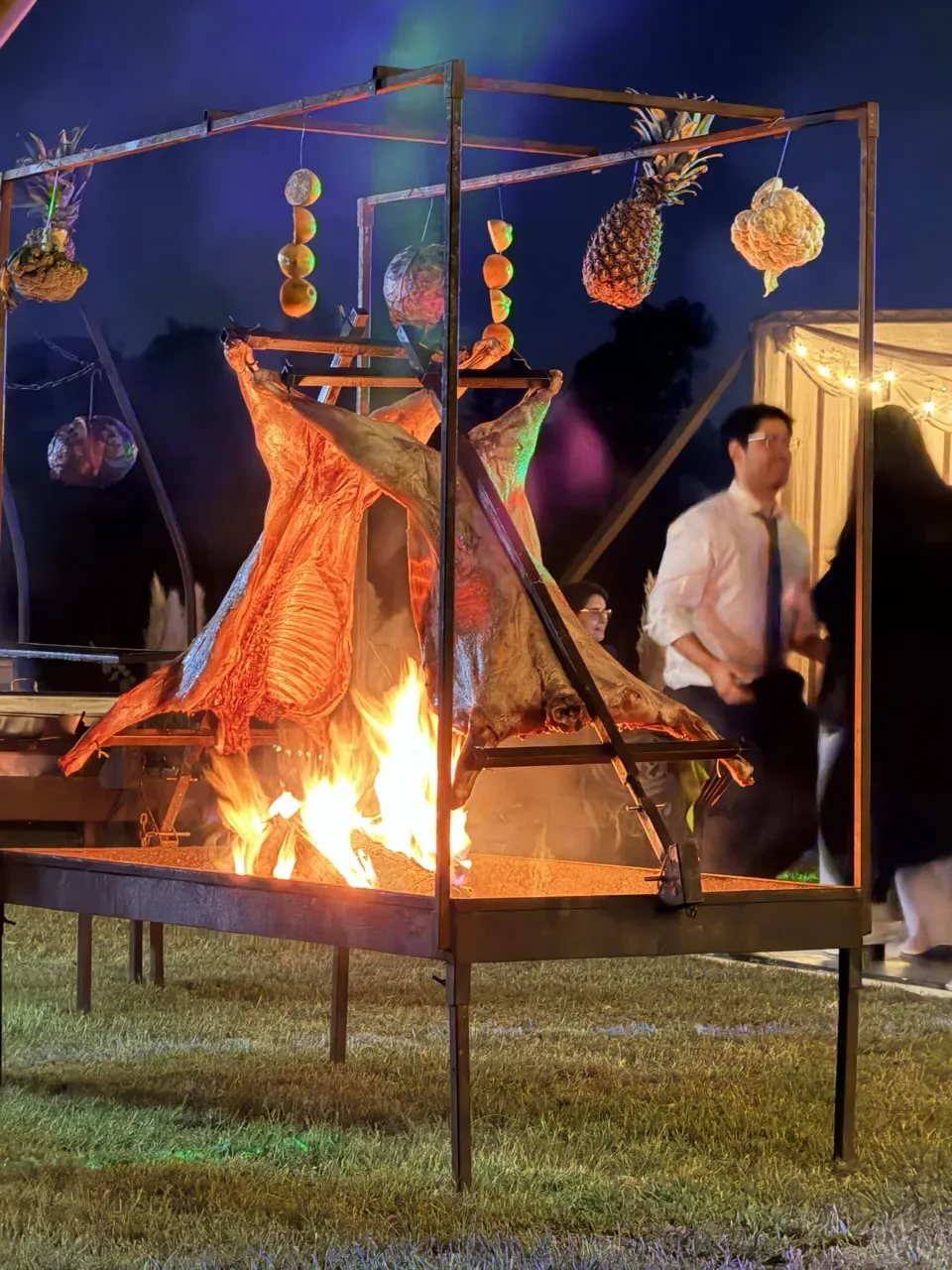 Dos corderos asándose a la cruz sobre el fuego en un evento nocturno — asado en vivo de Matías al Fuego